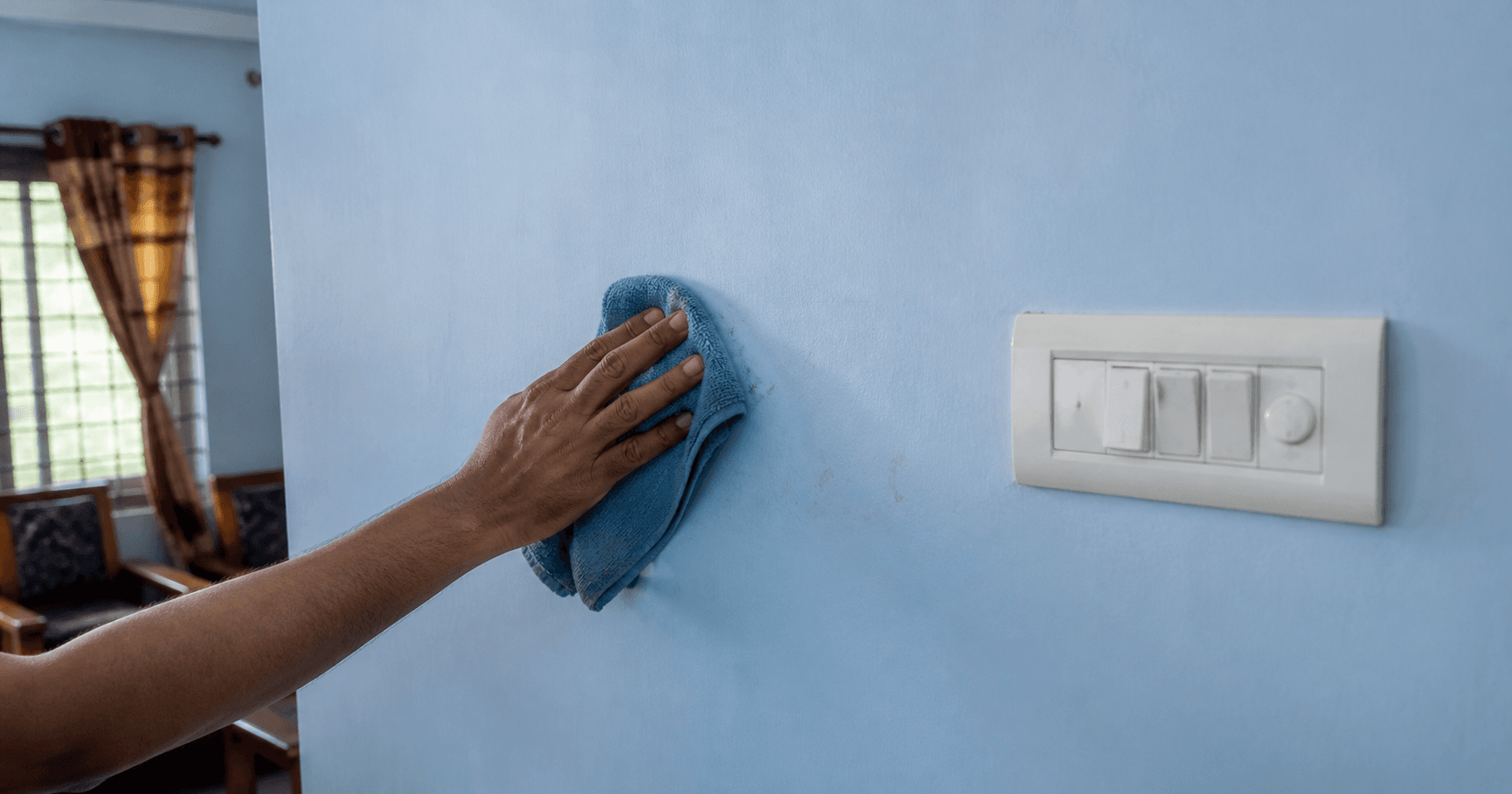 A living room wall in satin being wiped clean with a cloth near a light switch